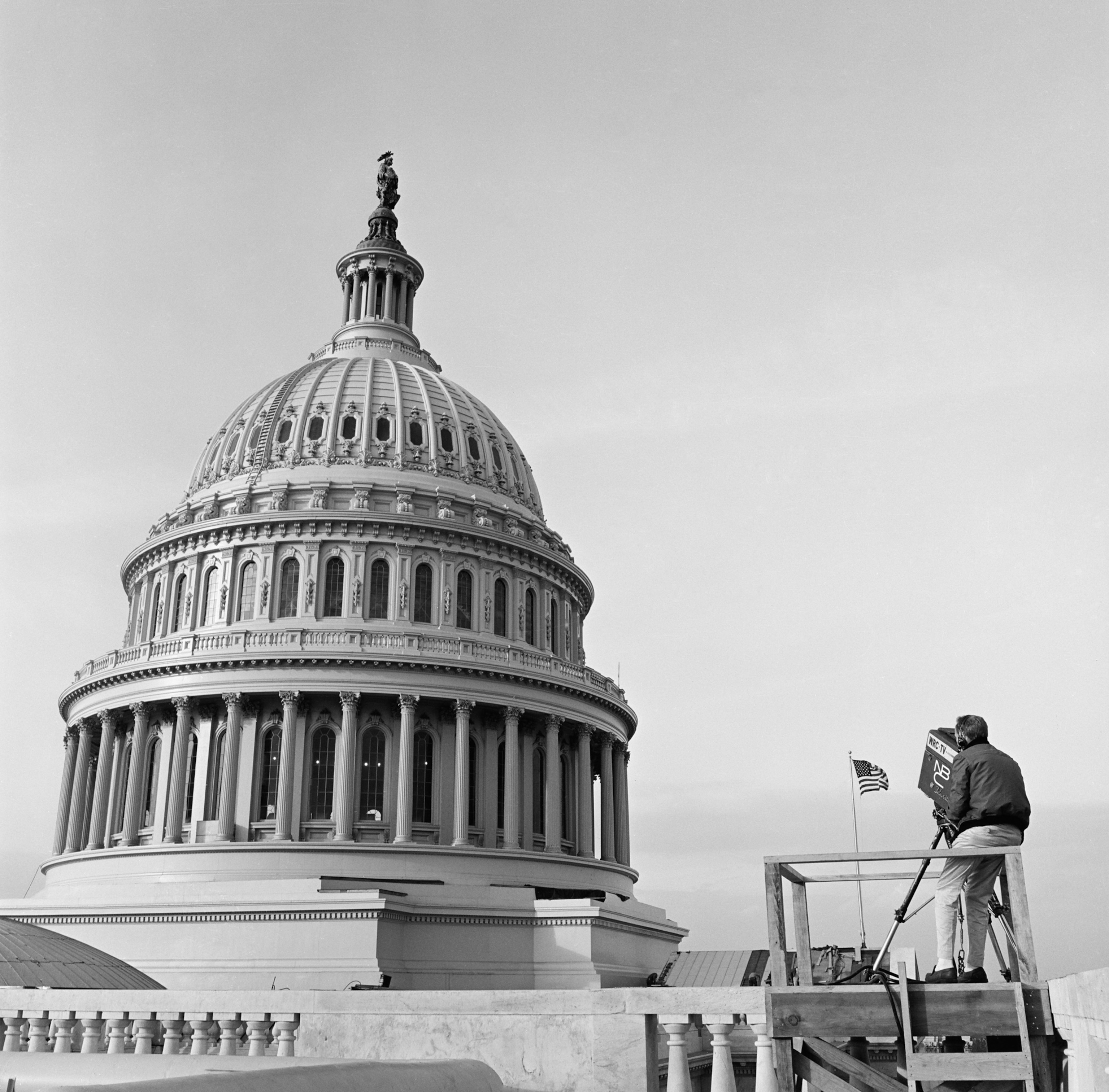 a cameraman sitting on the edge of a balcony near the U.S. Capitol