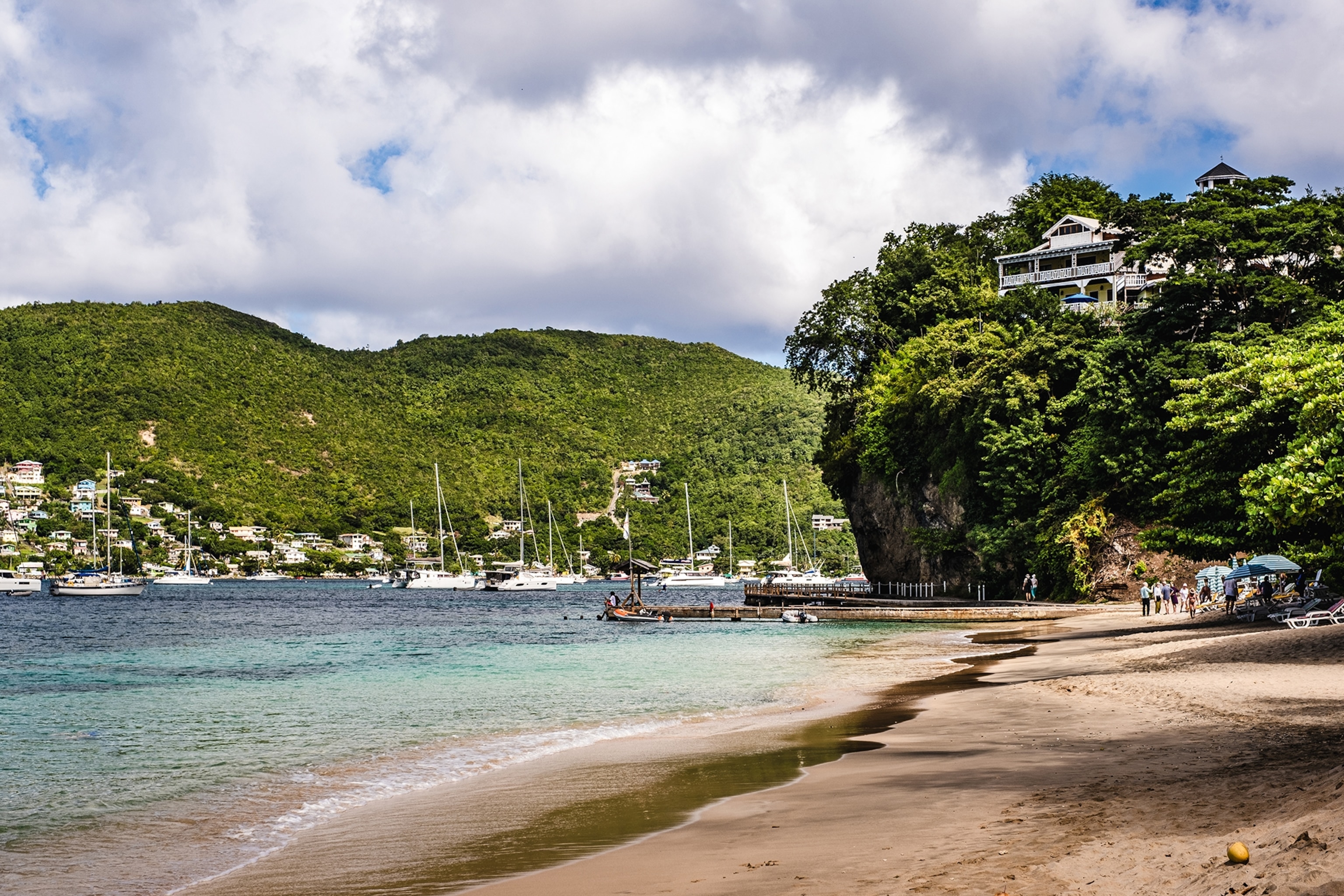 A quiet beach with a rock formation cutting in that looks like a green island with a colonial-style house.