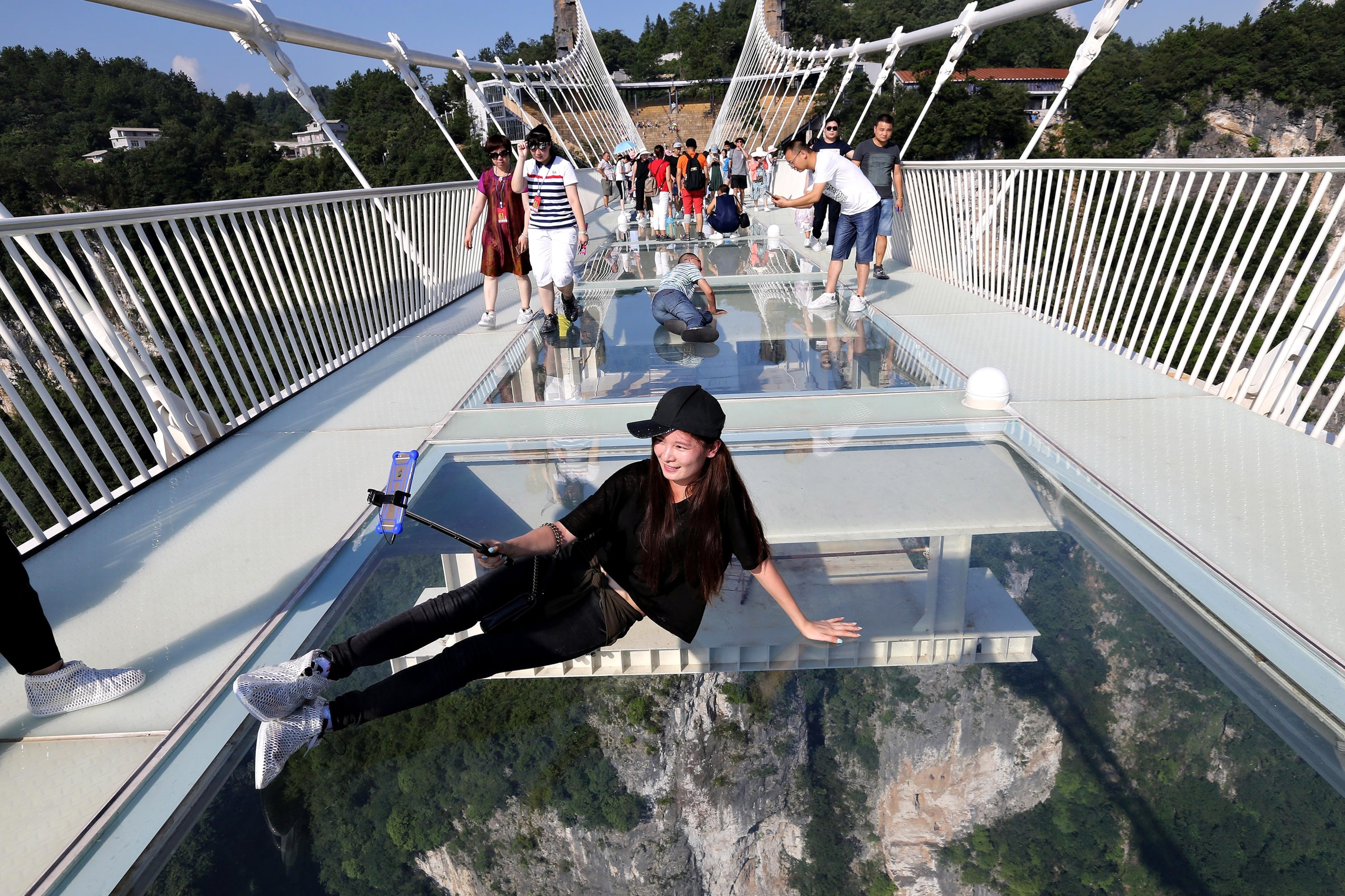 a tourist takes a selfie on the glass-bottom bridge at Zhangjiajie Grand Canyon, China