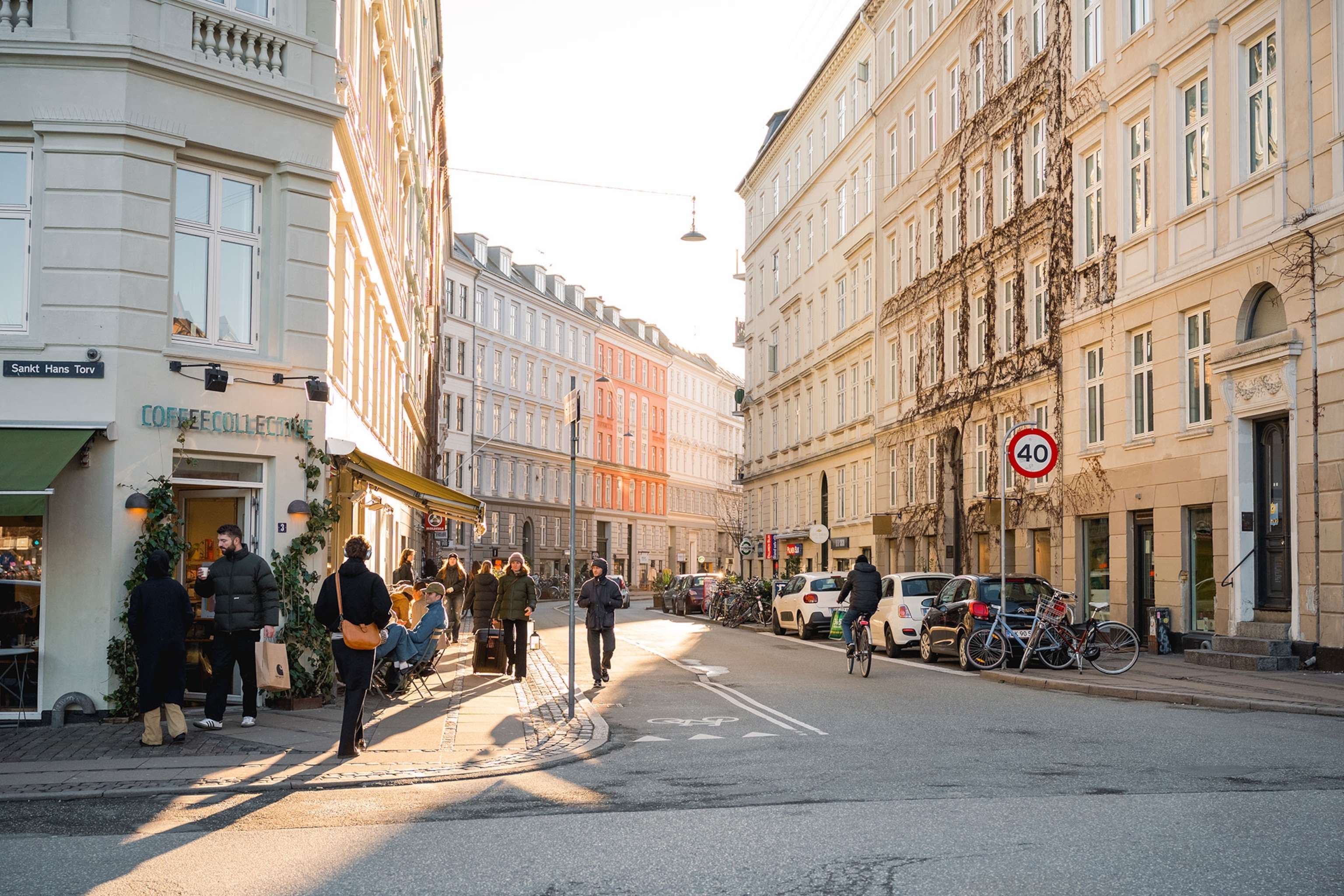 Pedestrians are seen walking down a colourful street in Copenhagen and standing outside a coffee shop.