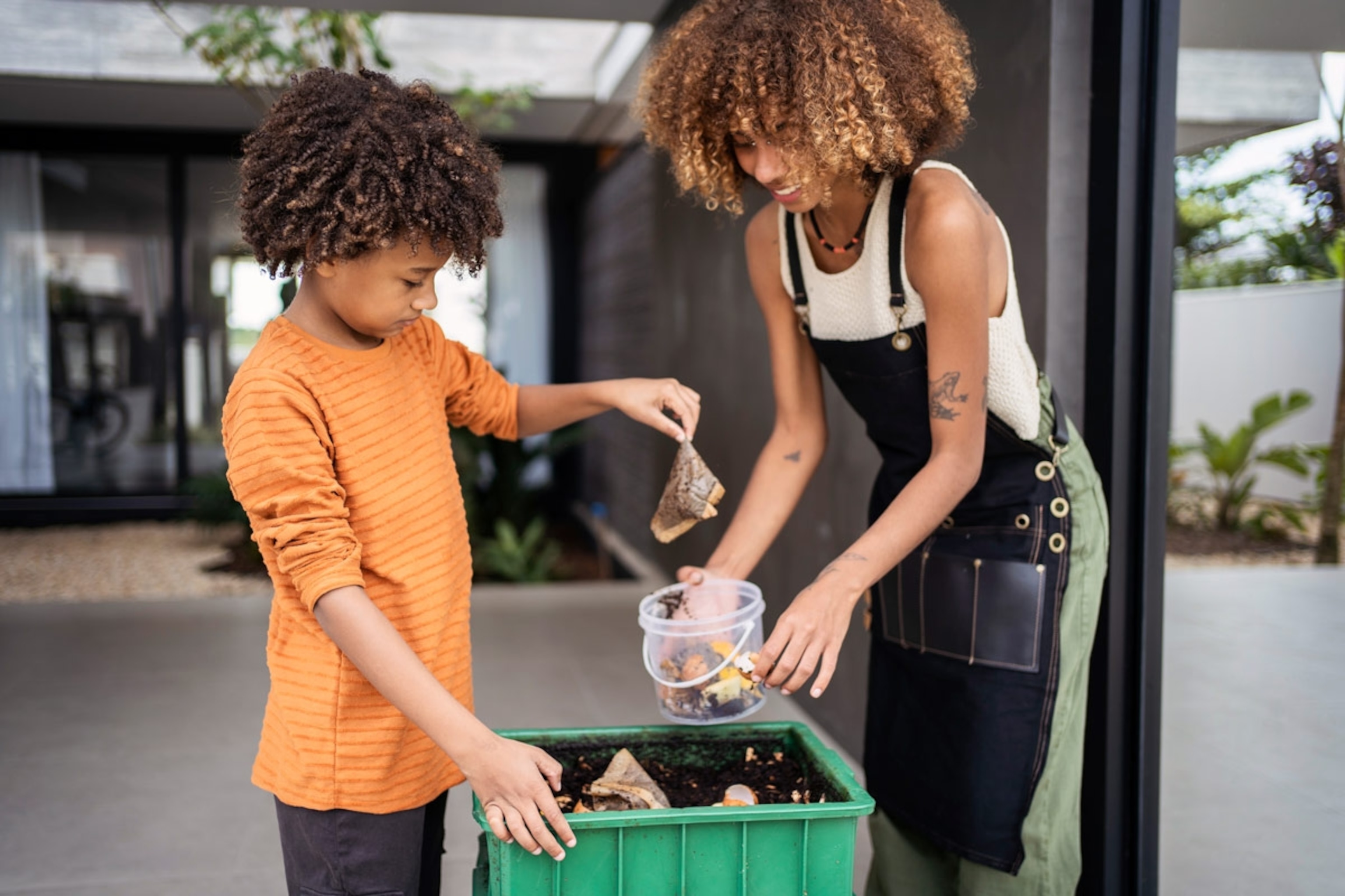 Young woman and her younger brother making compost from kitchen food leftovers into rich organic soil fertilizer.