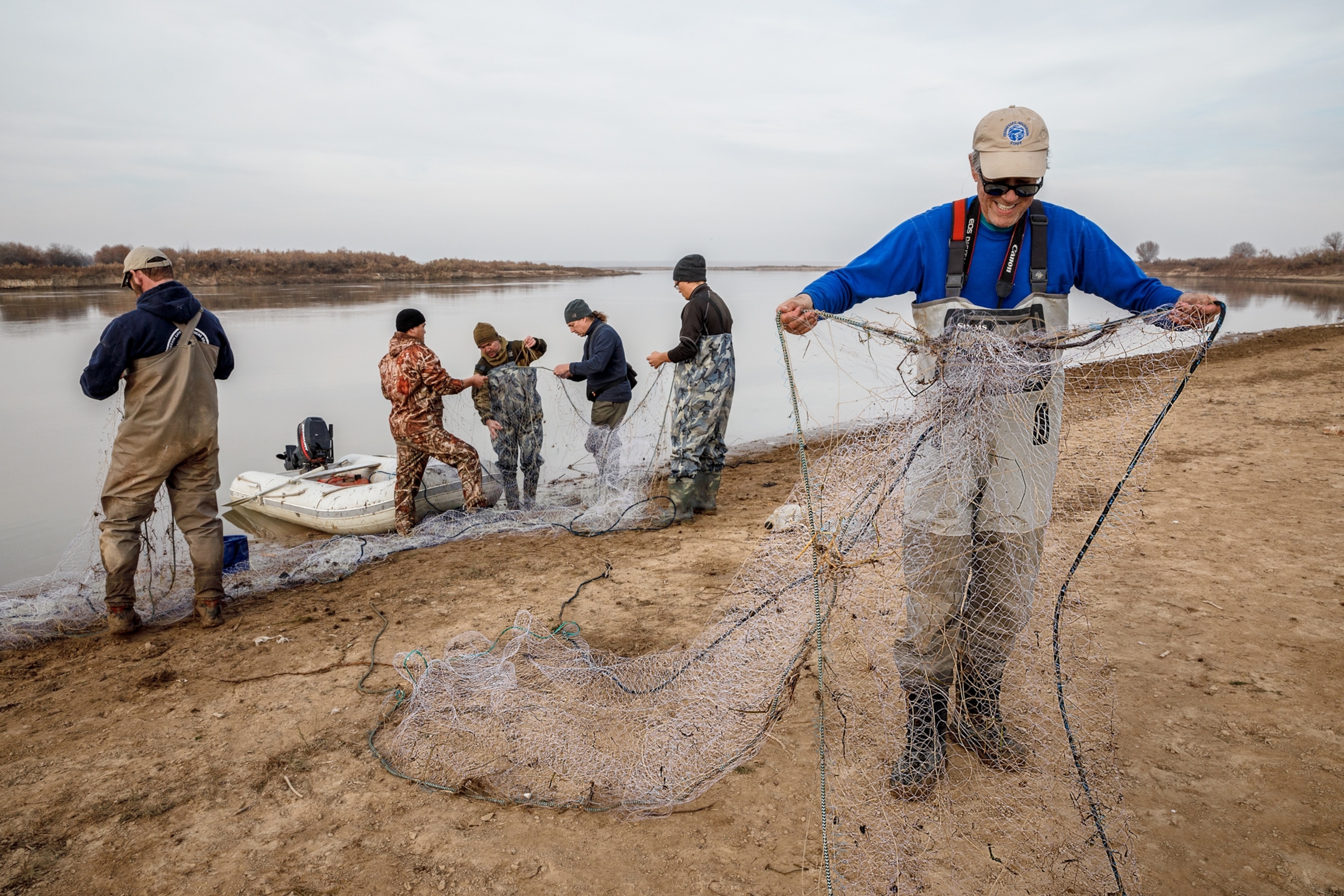 Six men stand at the foot of a river holding out large nets.