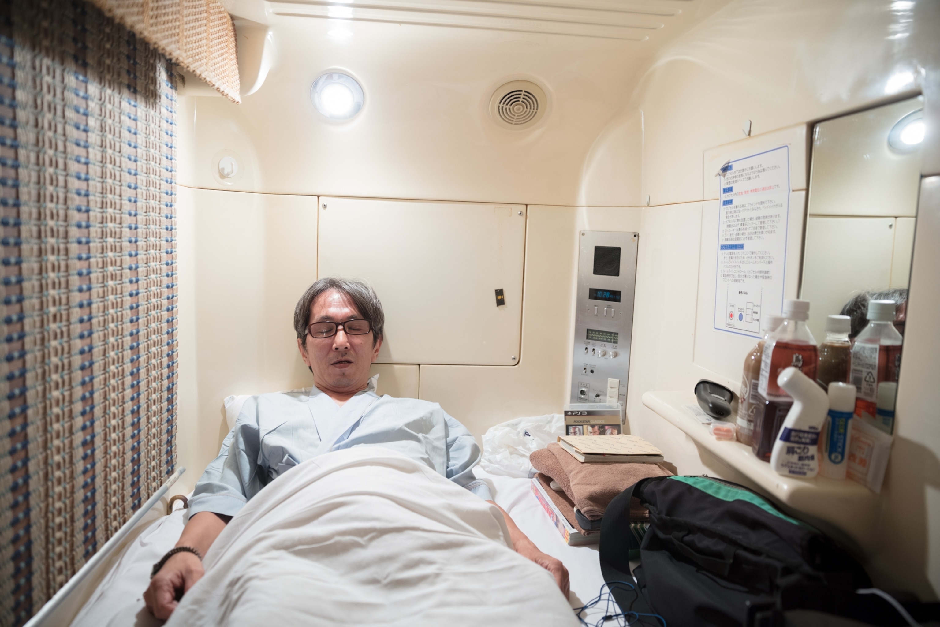 a man sleeping in tight quarters with a ledge in his capsule area holding toiletries