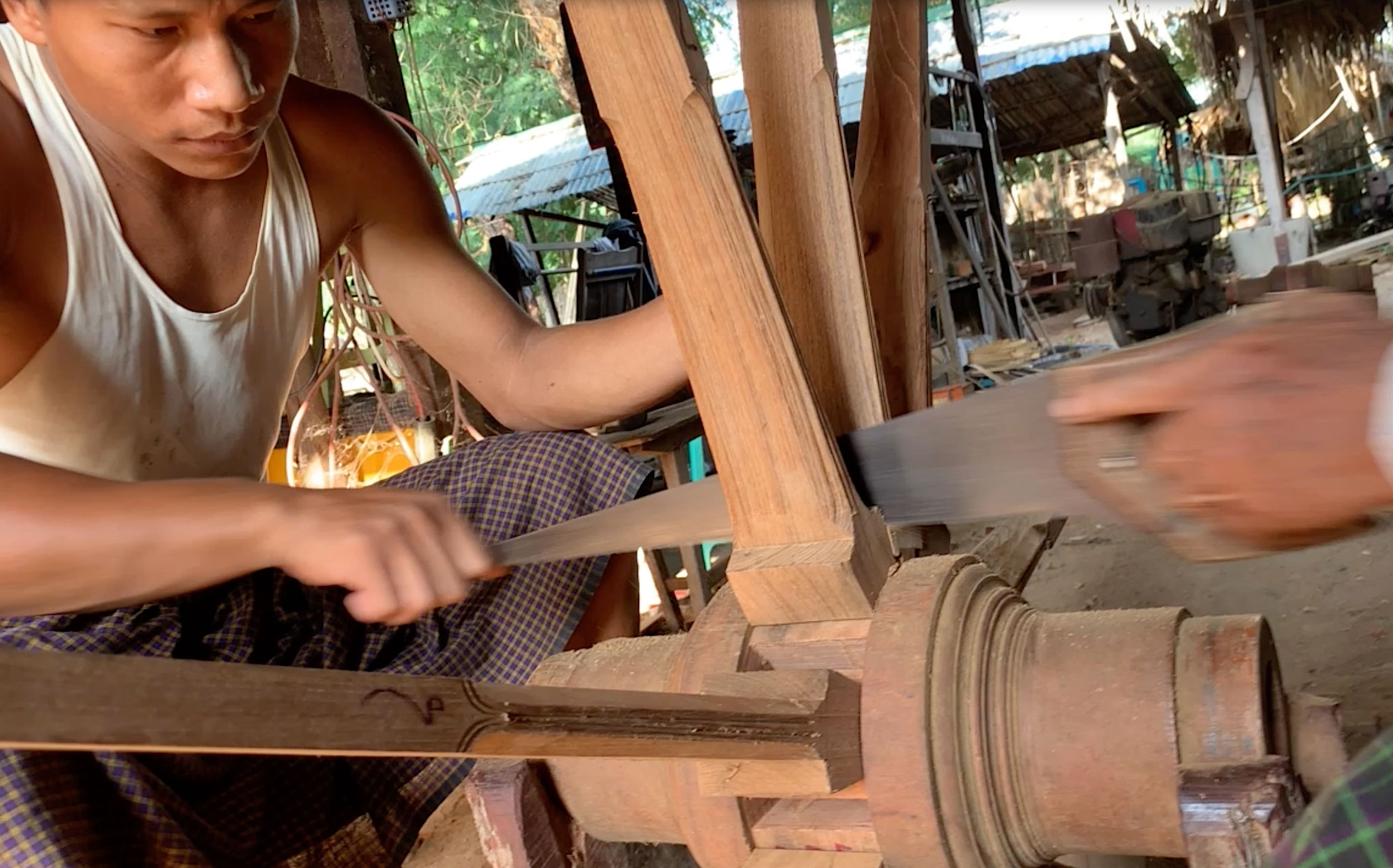 Two men saw between spokes on a wooden wheel