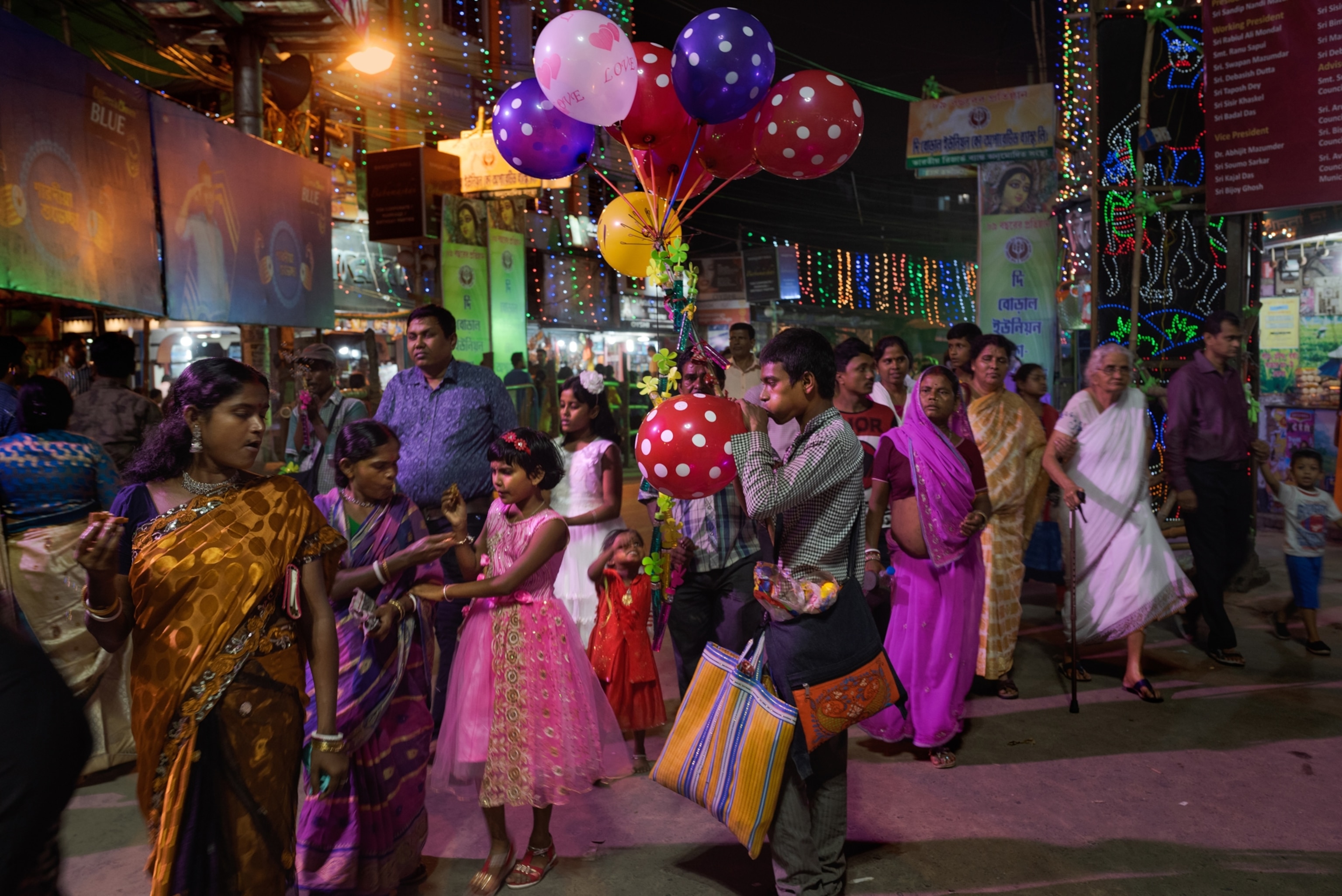 a group of people walk past a person blowing up a balloon at an outdoor festival