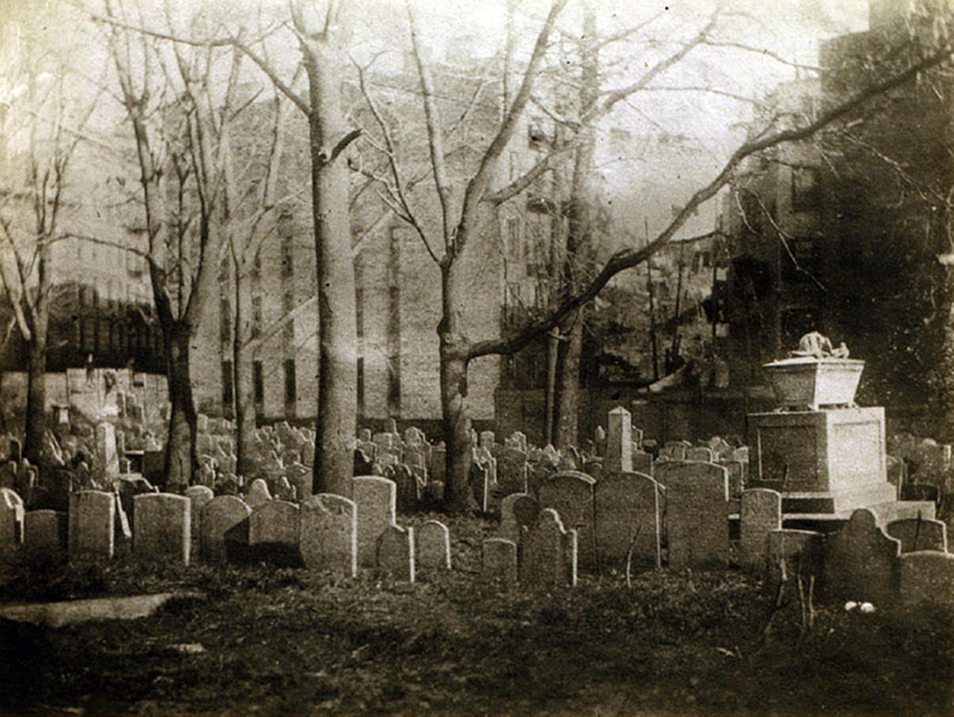 A black and white image of a graveyard which sits amongst a city.