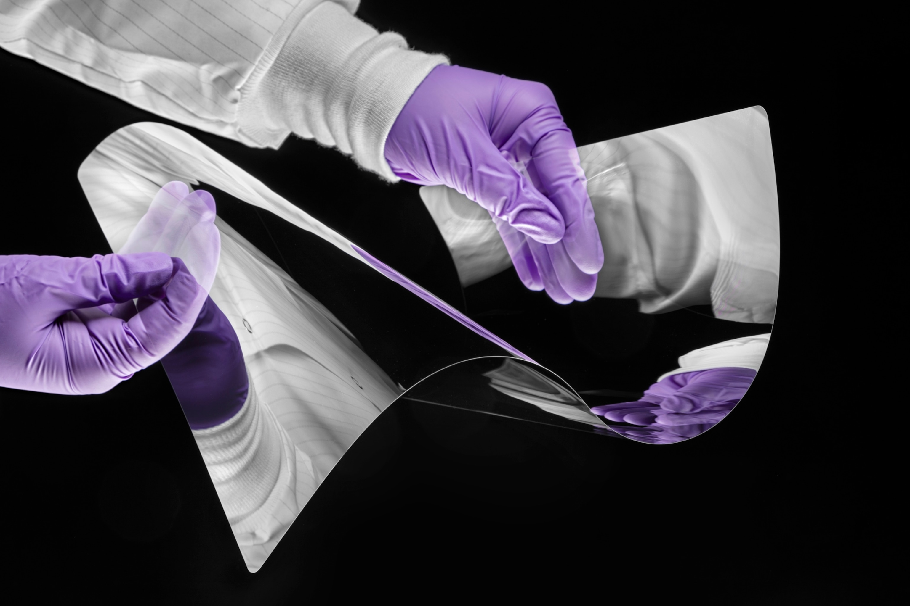 two arms in a white lab coat and purple latex gloves bends a reflective piece of glass in a wave pattern.