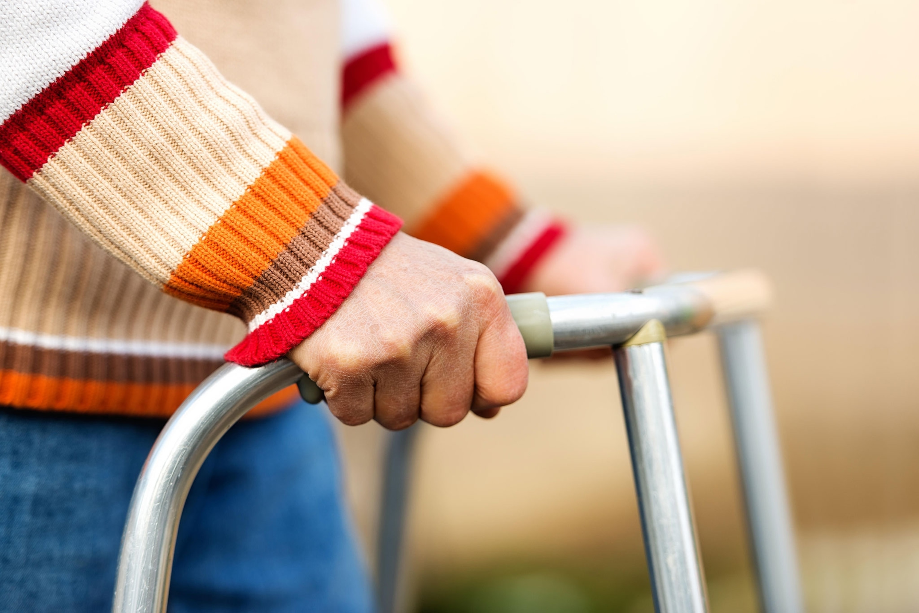 A close up of a person in a red, orange and brown striped sweater using a walker.