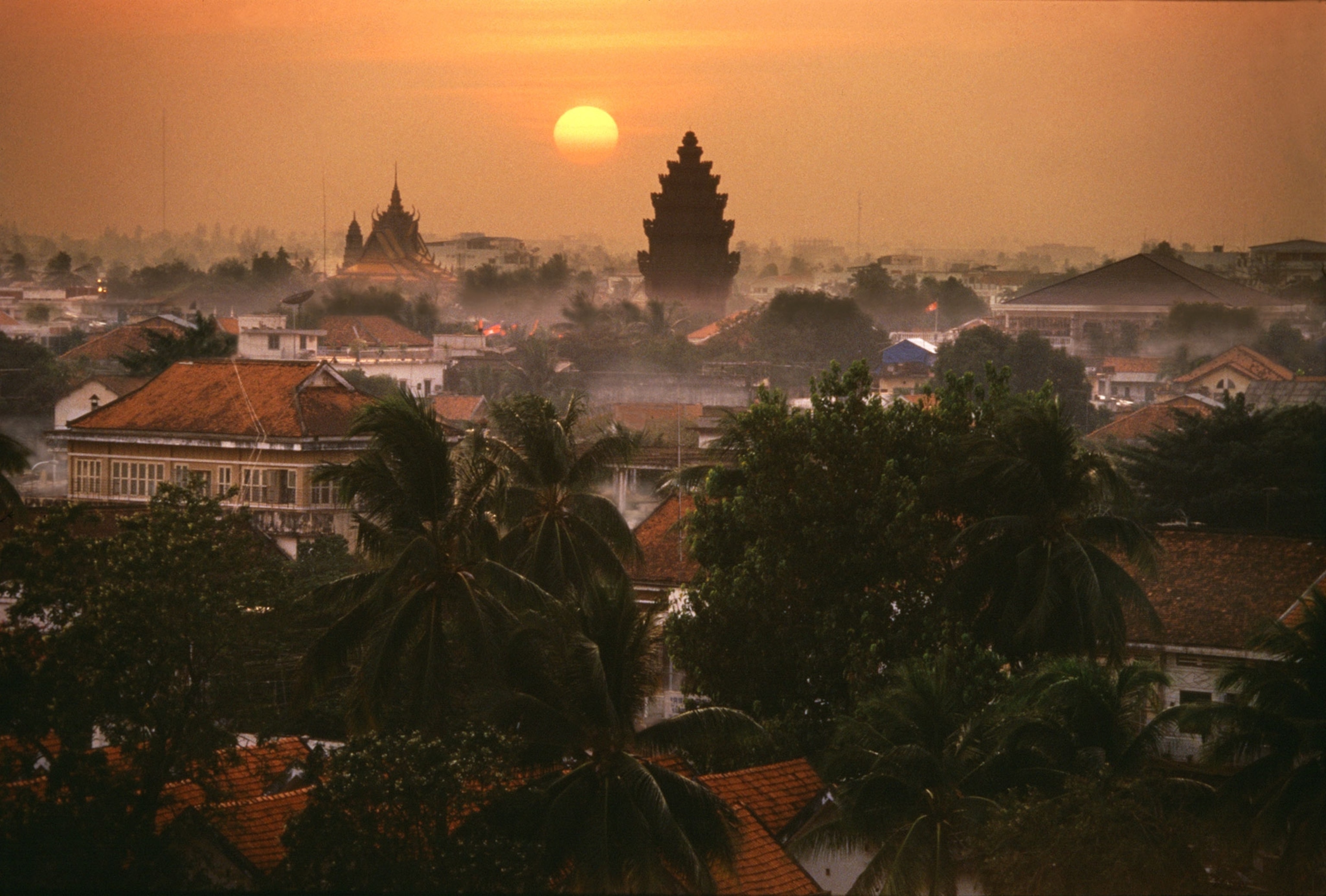 Phnom Penh with the Independence Monument at sunset and palm trees hovering over homes and buildings