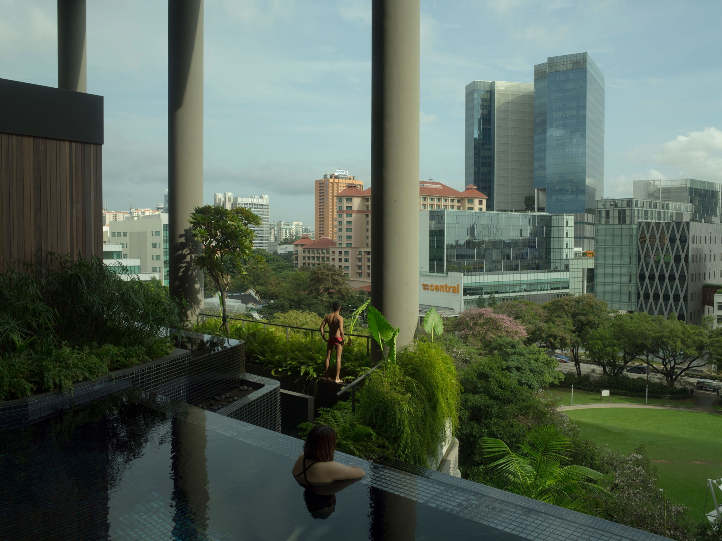 a person in an infinity pool surrounded by green space and a city skyline